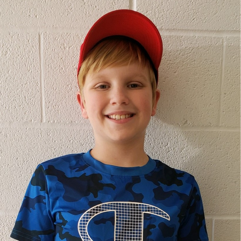 smiling boy  with blonde hair wearing a red cap and blue camo shirt
