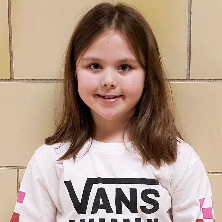 smiling young girl with brown hair  wearing a white shirt with the word VANS on it