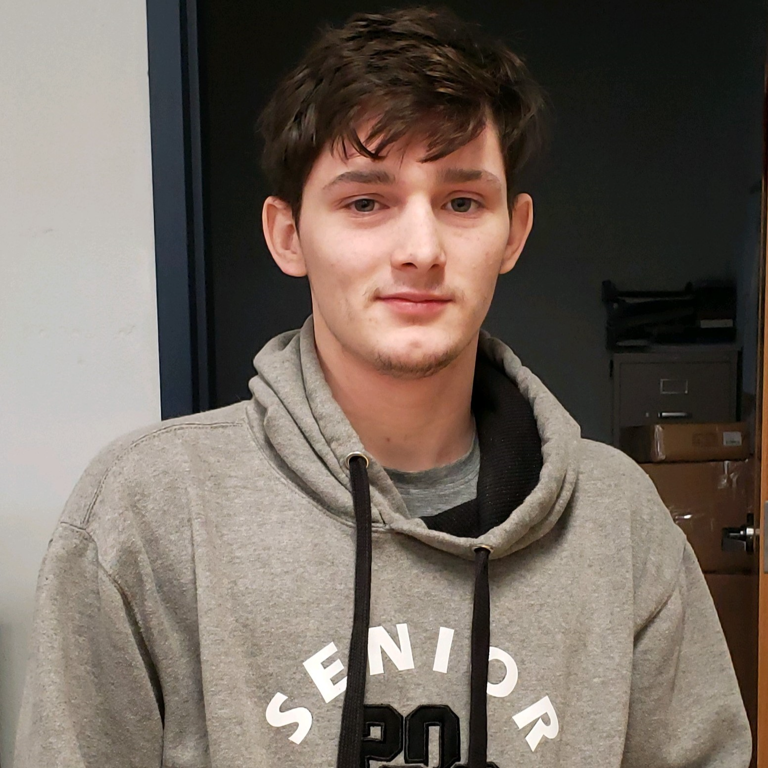 smiling young man with brown hair wearing a gray hoodie 