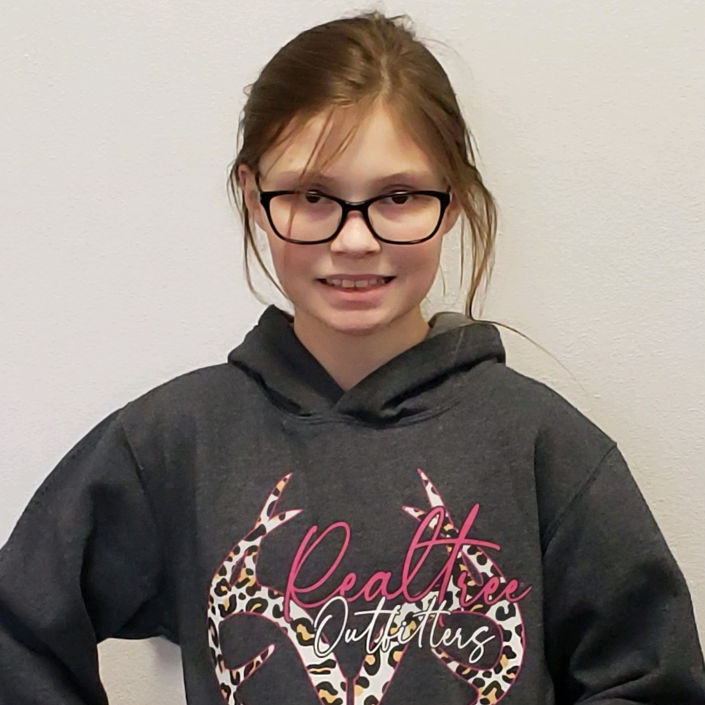 grinning young lady with dark blonde hair pulled back  and  glasses wearing a gray hoodie with antlers and Realtree on it