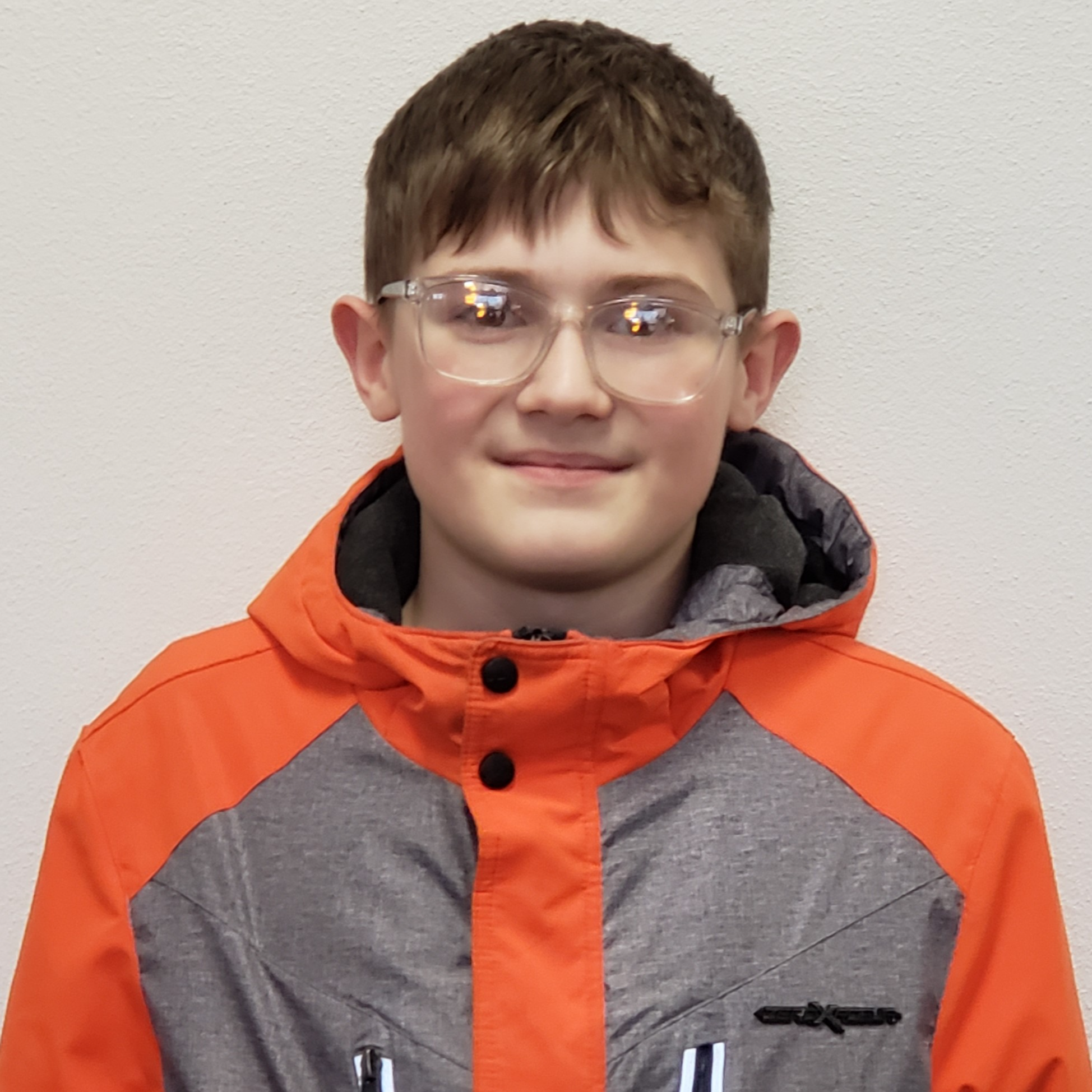 boy with light-brown hair wearing clear-rimmed glasses and a gray-&-orange jacket with a hood