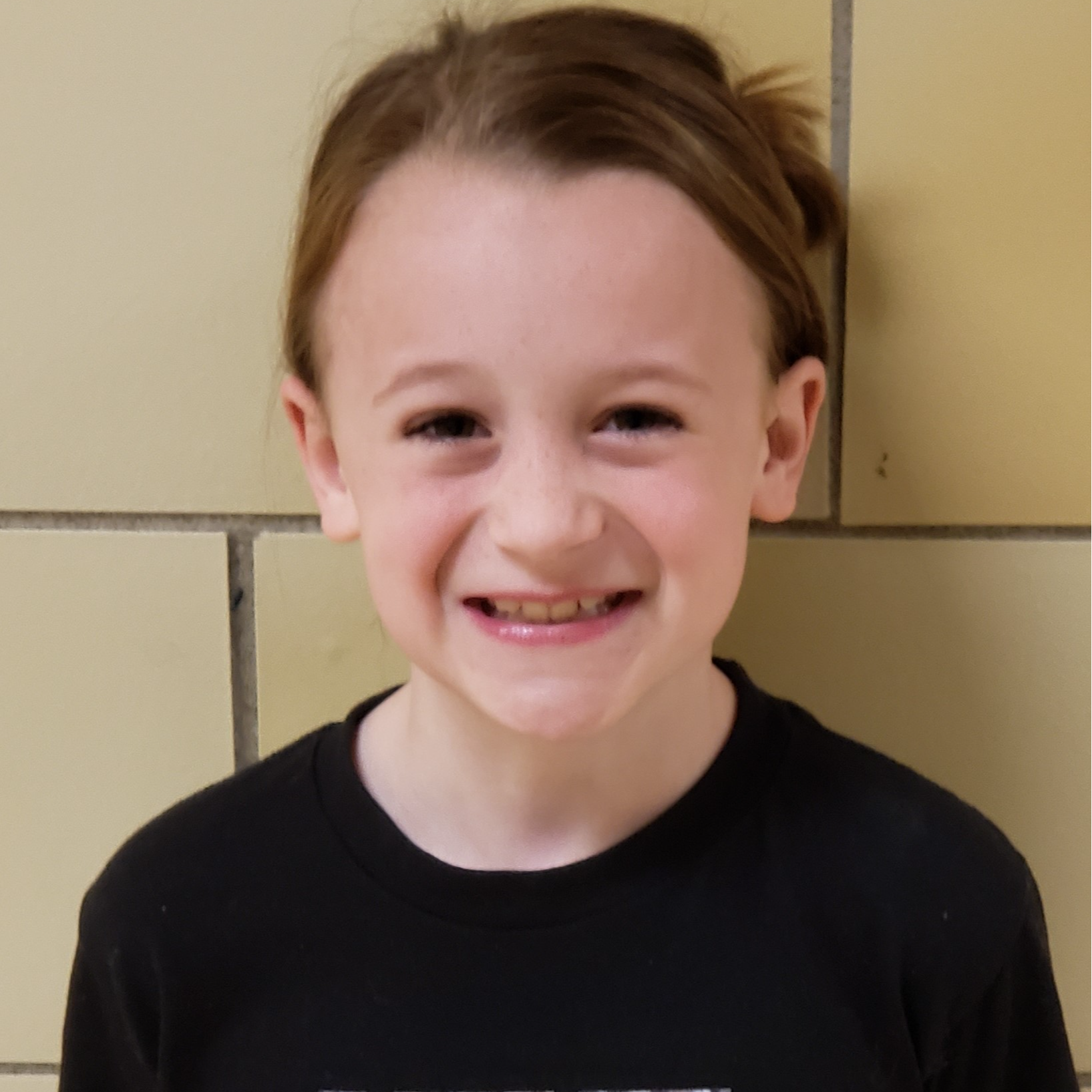 smiling girl with light brown hair pulled back wearing a black t-shirt