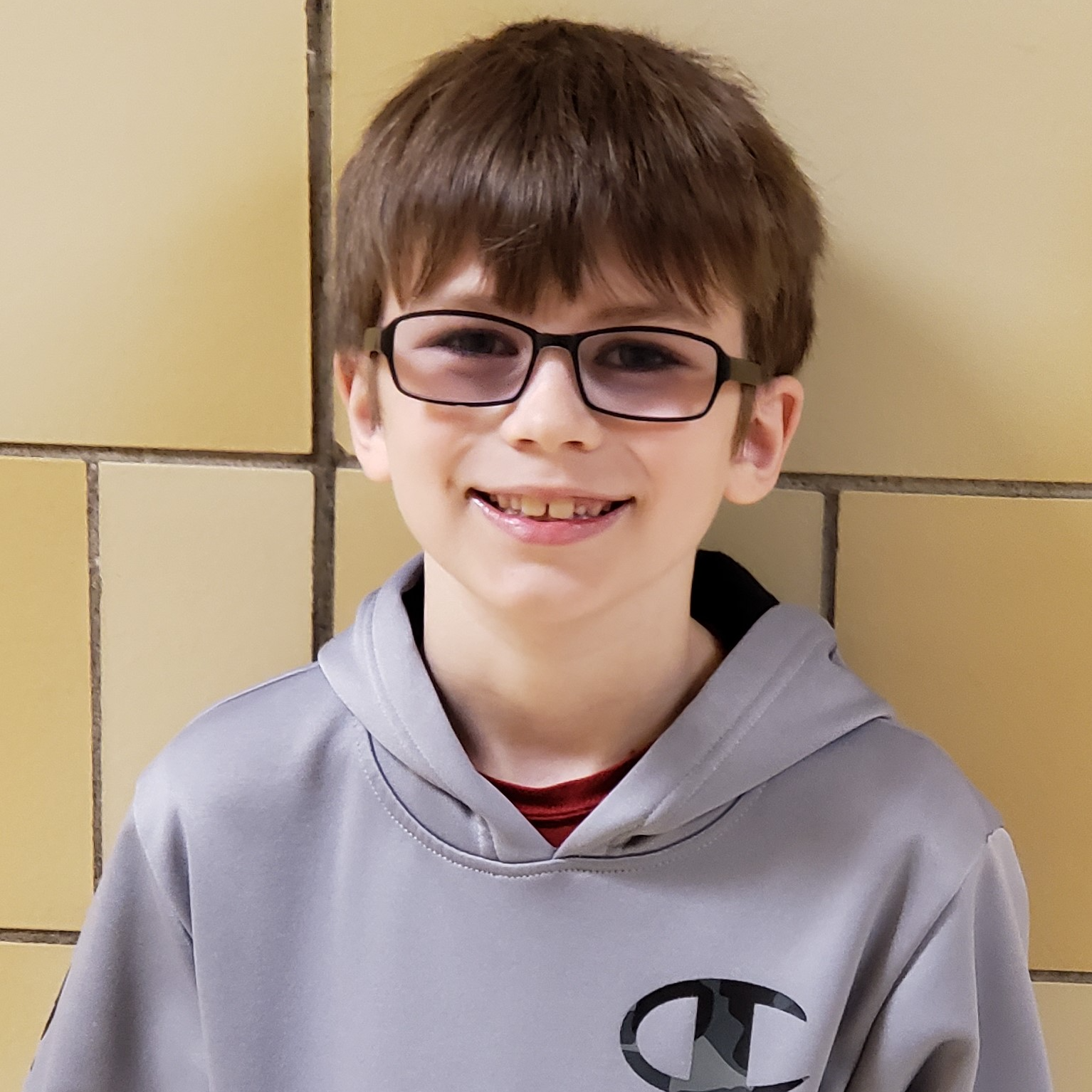 smiling boy with brown hair wearing a black-rimmed glasses and a gray hooded sweatshirt