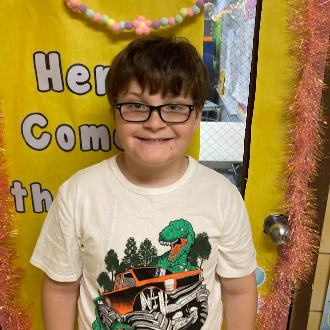 smiling boy with brown hair and glasses with a t-rex monster truck t-shirt