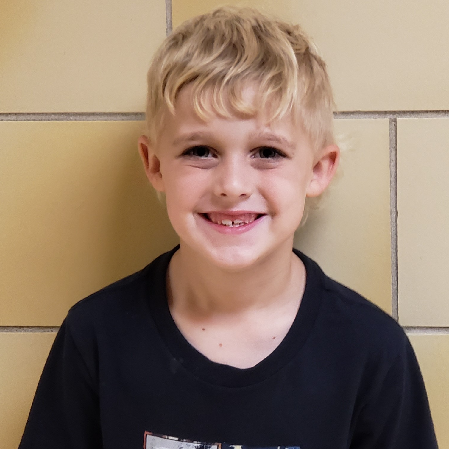 smiling young boy with blonde hair wearing a black t-shirt
