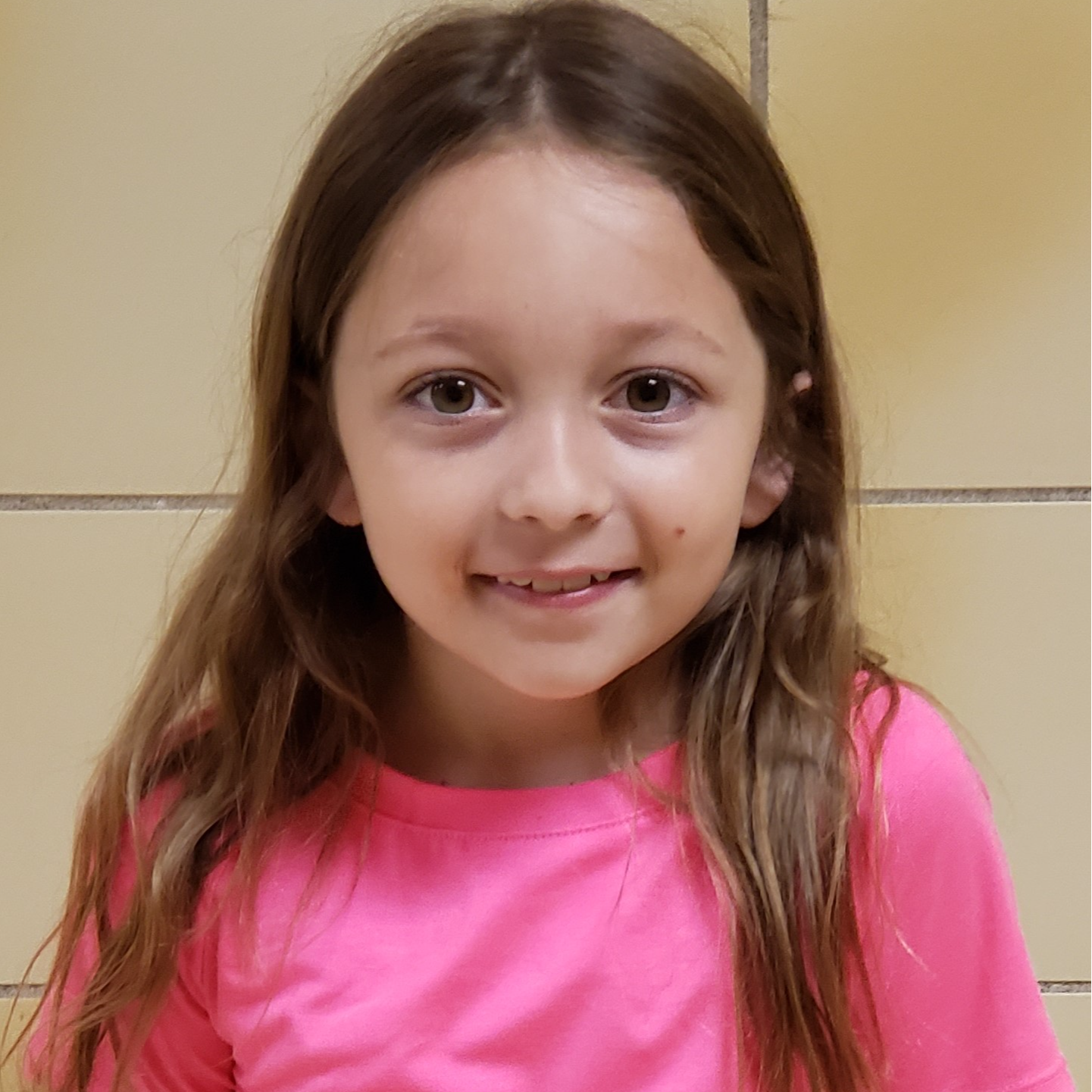 young girl with long brown hair wearing a pink t-shirt