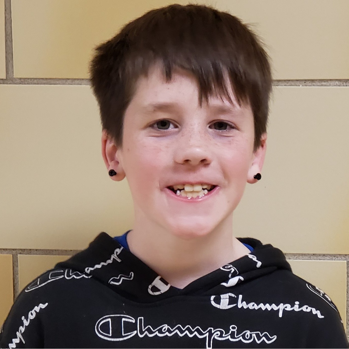 smiling young boy with dark brown hair wearing black earrings and a black hoodie