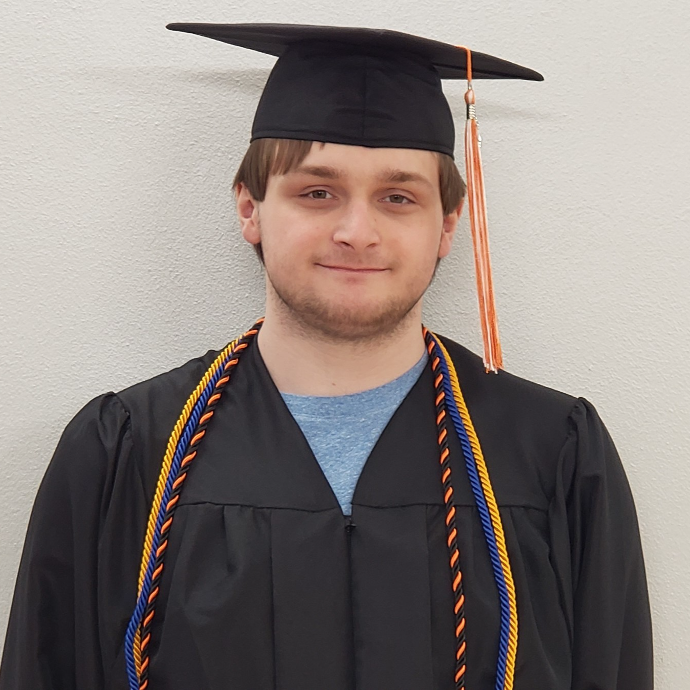 Young man with brown hair wearing a black graduation cap & gown with blue & gold and orange & black cords