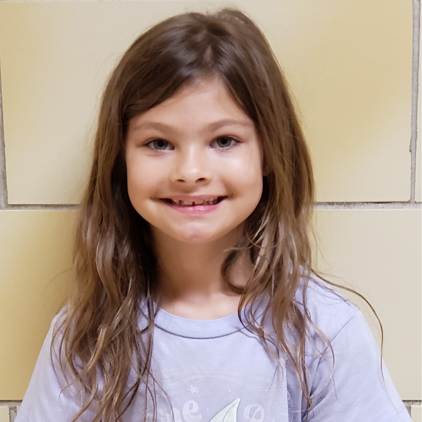 smiling young girl with brown hair  wearing a light purple t-shirt