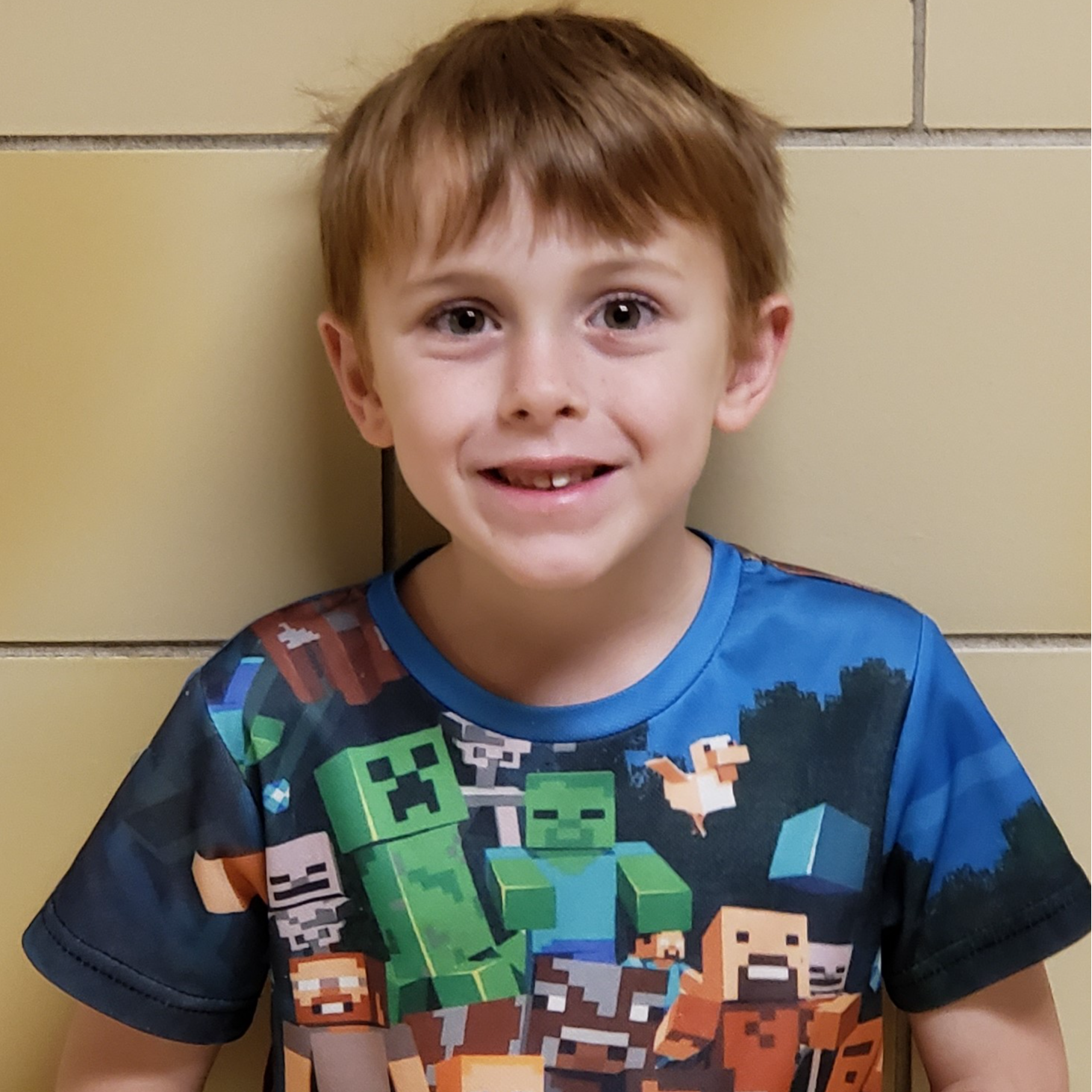 young boy with dark blonde hair wearing a roblox t-shirt