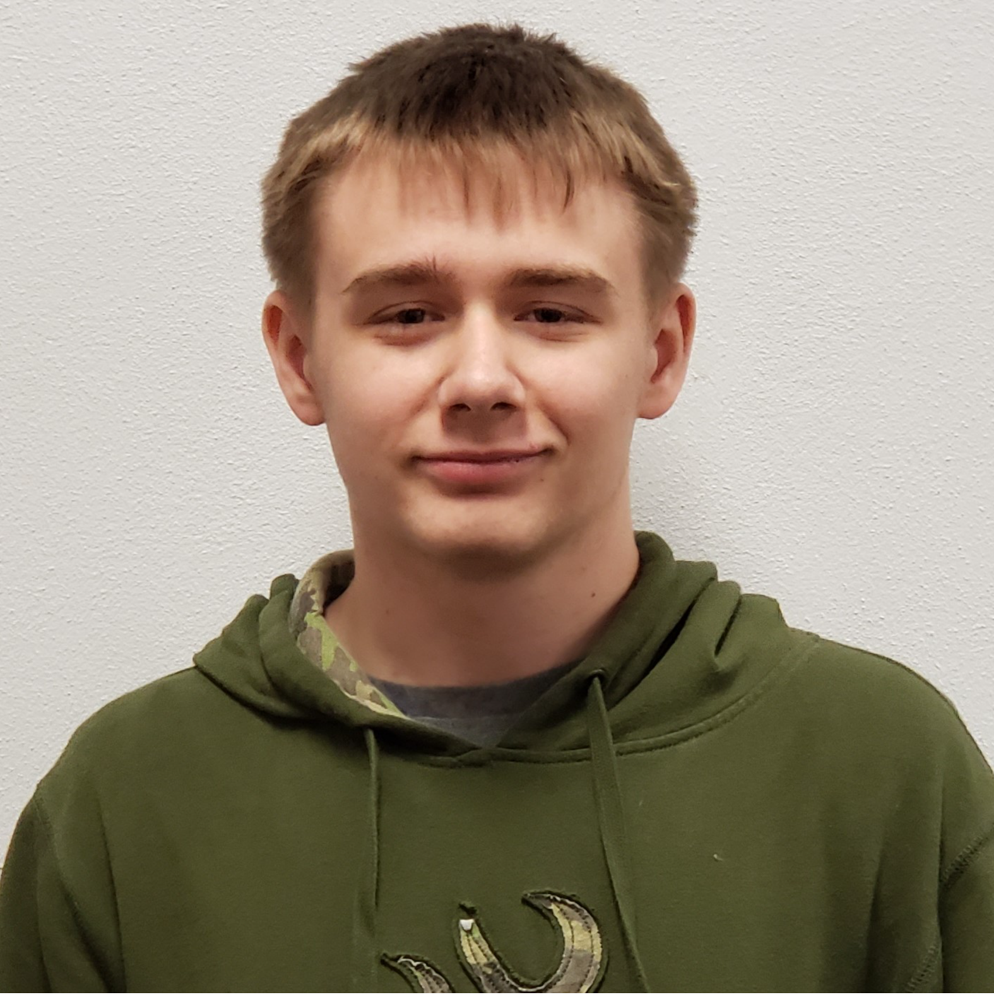 young man with dark blonde hair wearing an olive green hoodie