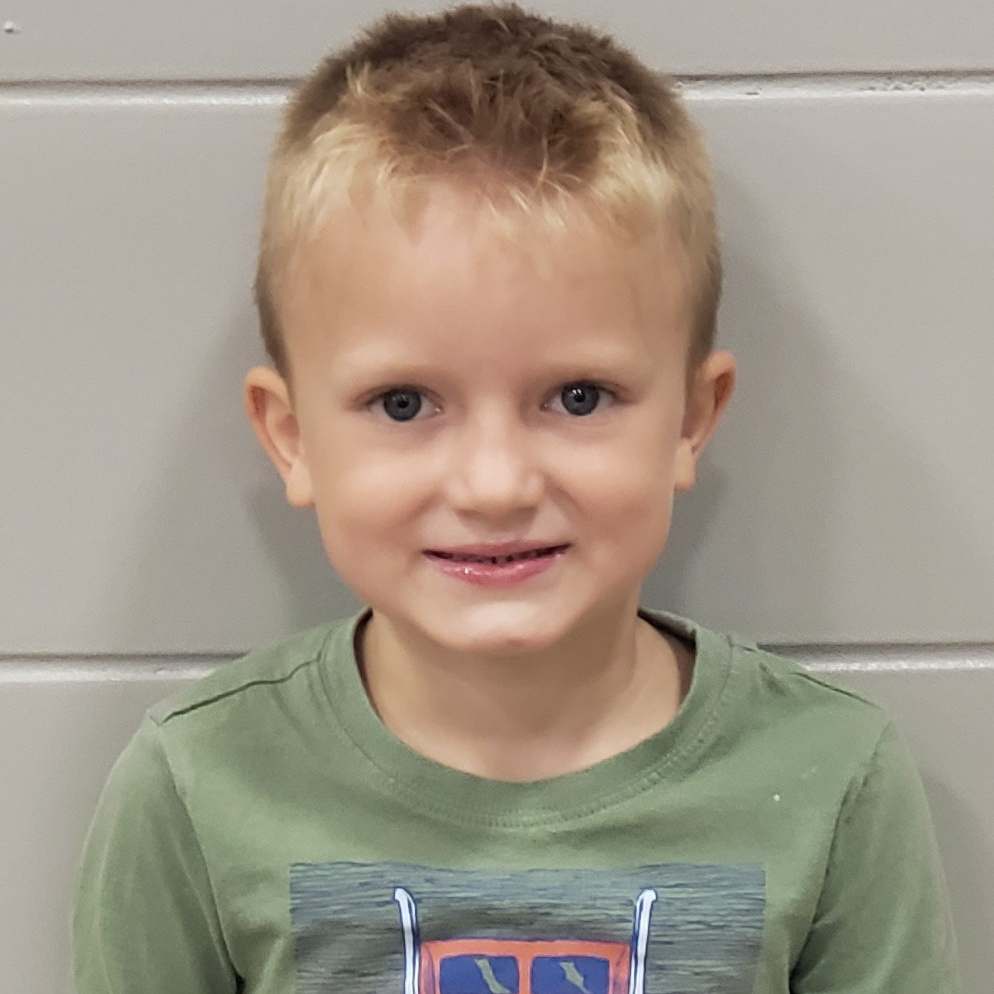 smiling little boy with blonde spiky hair wearing a green t-shirt