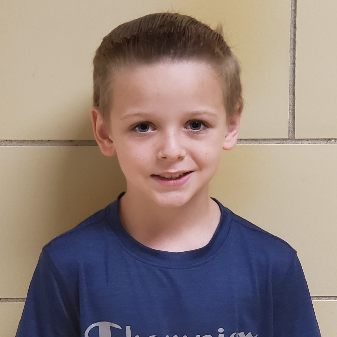 smiling boy with dark blonde hair spiked in the front wearing a  navy bluet-shirt