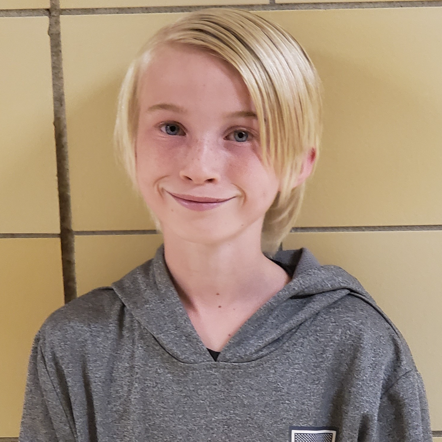 smiling boy with light blonde hair parted on the side wearing a gray hoodie