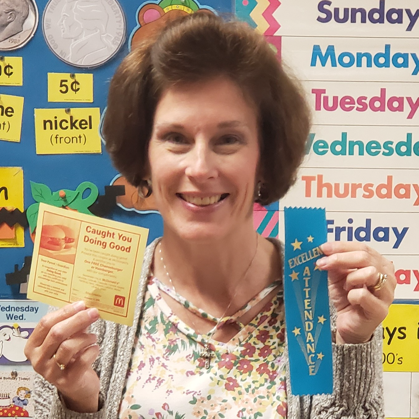 female teacher with reddish brown hair wearing a flowered t-shirt under a tan cardigan