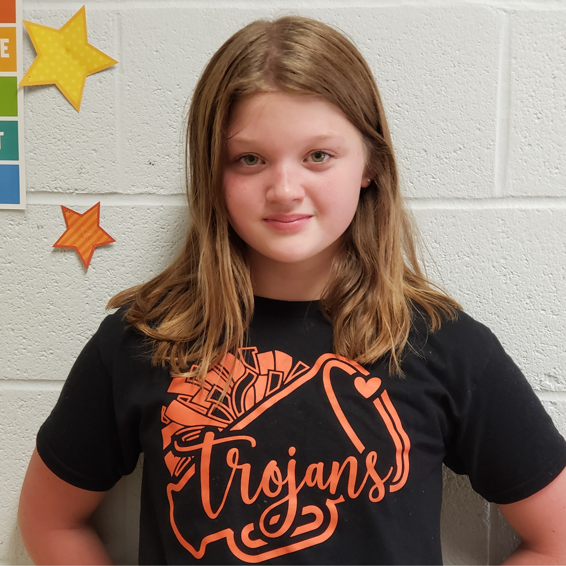 girl with dark blonde shoulder-length hair wearing a black t-shirt with orange poms,  a megaphone, and Trojans on it