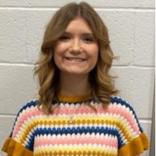 young lady with light brown hair wearing a striped sweater that has goldenrod, white, blue, and pink stripes