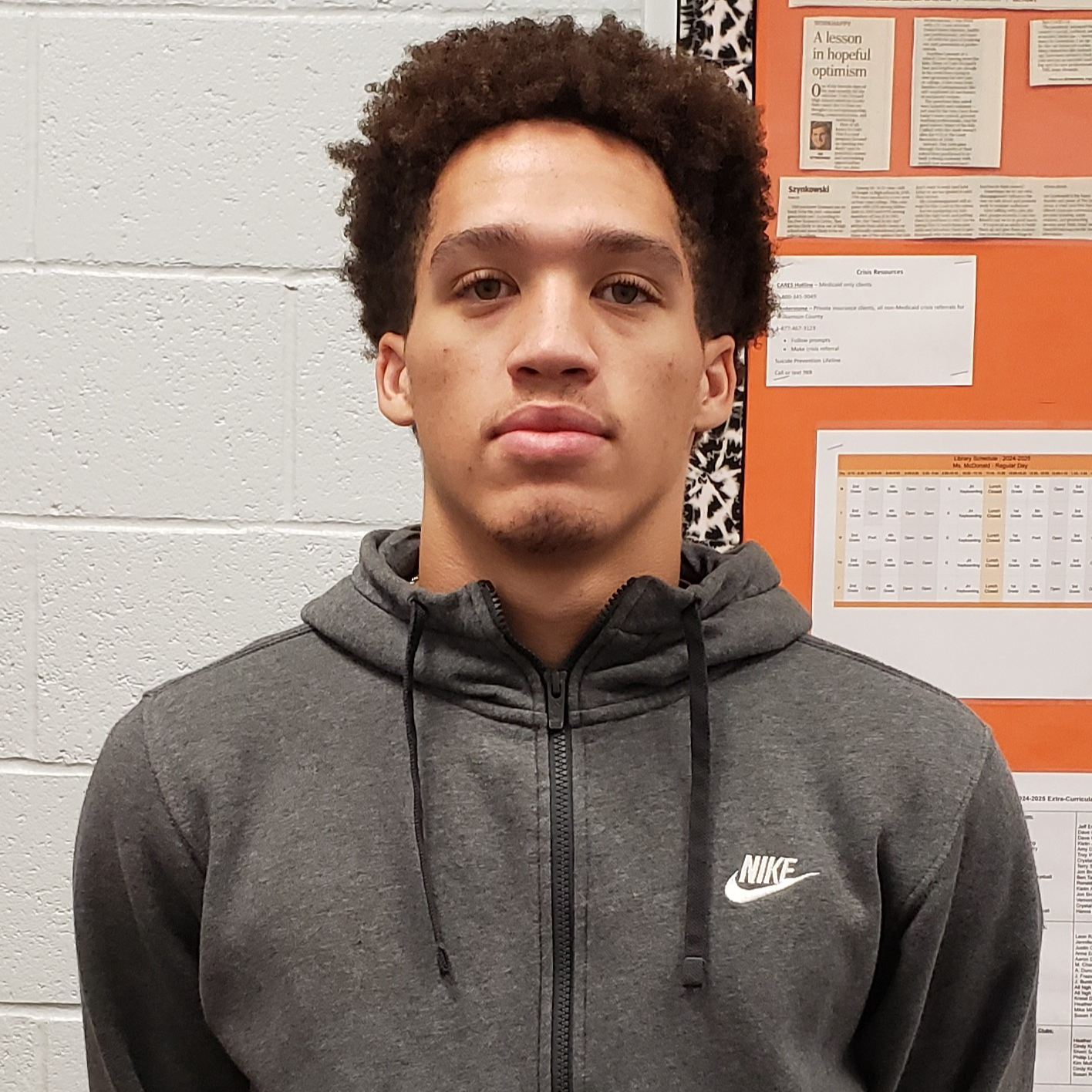 young man with curly brown hair wearing a gray zipped-up Nike jacket