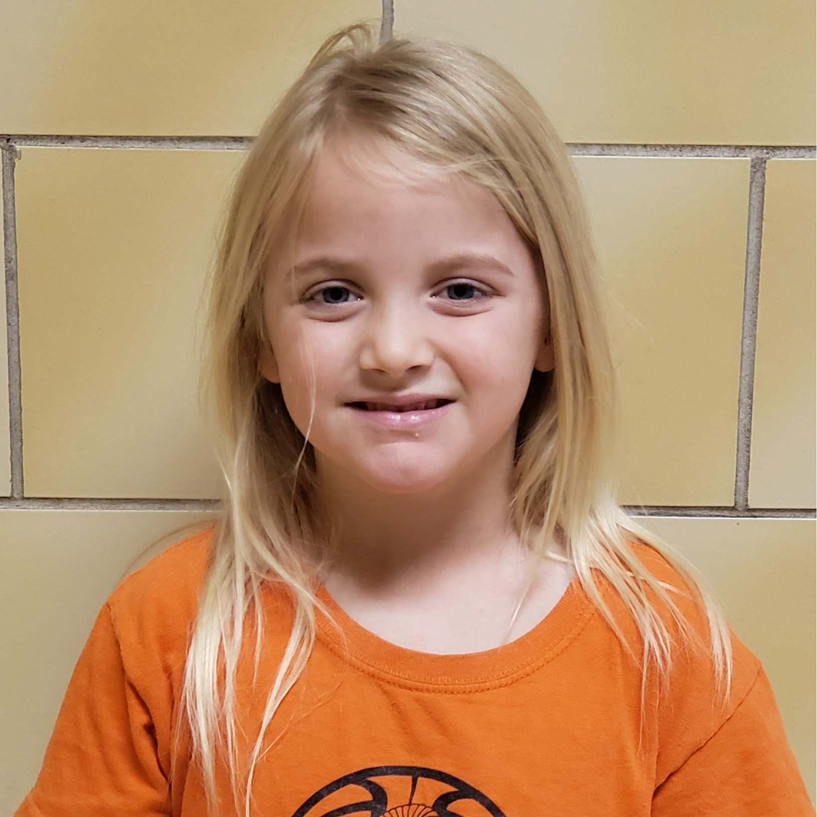 young girl with light blonde hair wearing an orange t-shirt