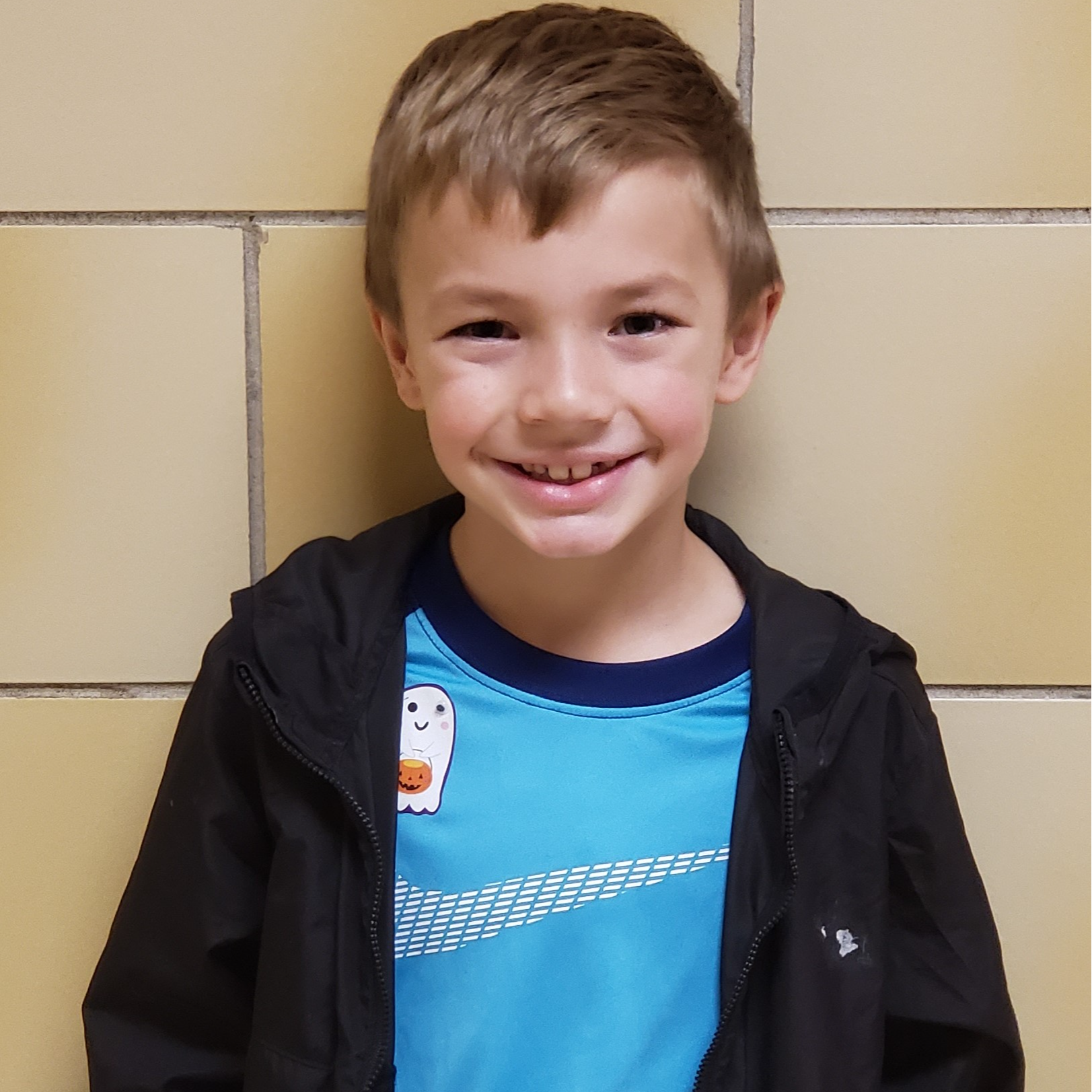 smiling little boy with light brown hair wearing a light blue shirt under a black unzipped jacket