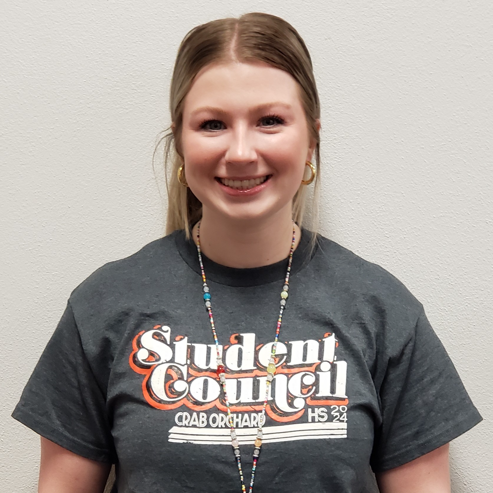 smiling female staff member with hair pulled back wearing a gray Student Council t-shirt