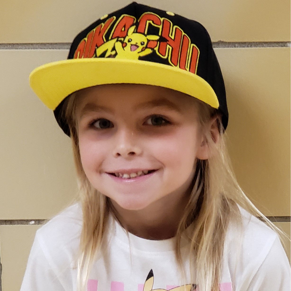 smiling little girl with light blonde hair wearing a pikachu hat and white t-shirt