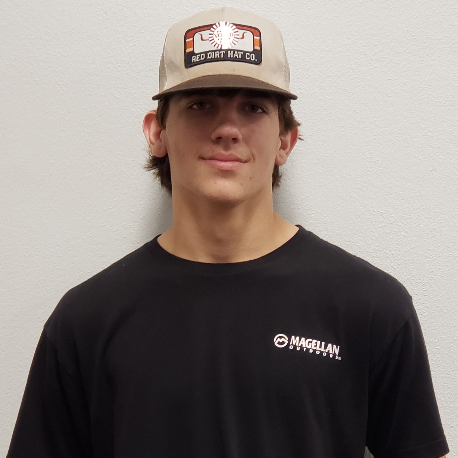 young man with brown hair wearing a tan cap and a black t-shirt