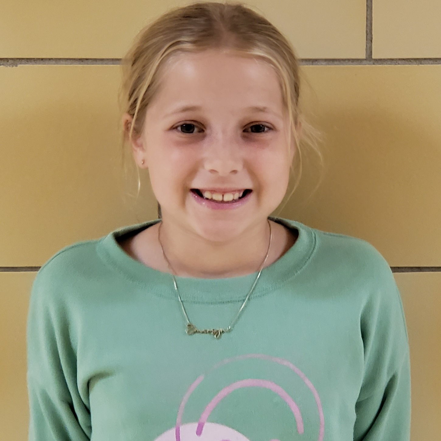 smiling girl with light blonde hair pulled back wearing a mint green sweatshirt