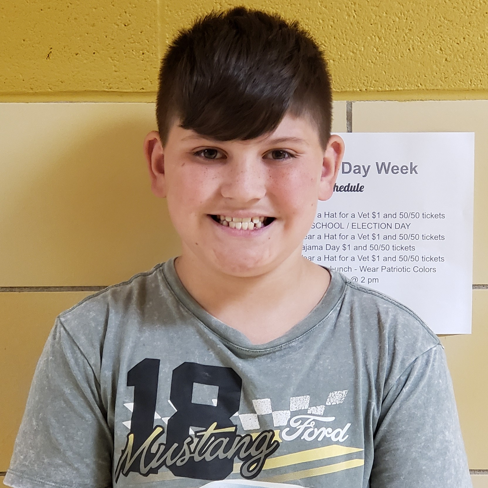 smiling boy with dark hair wearing a gray t-shirt with 18 Mustang Ford written on it