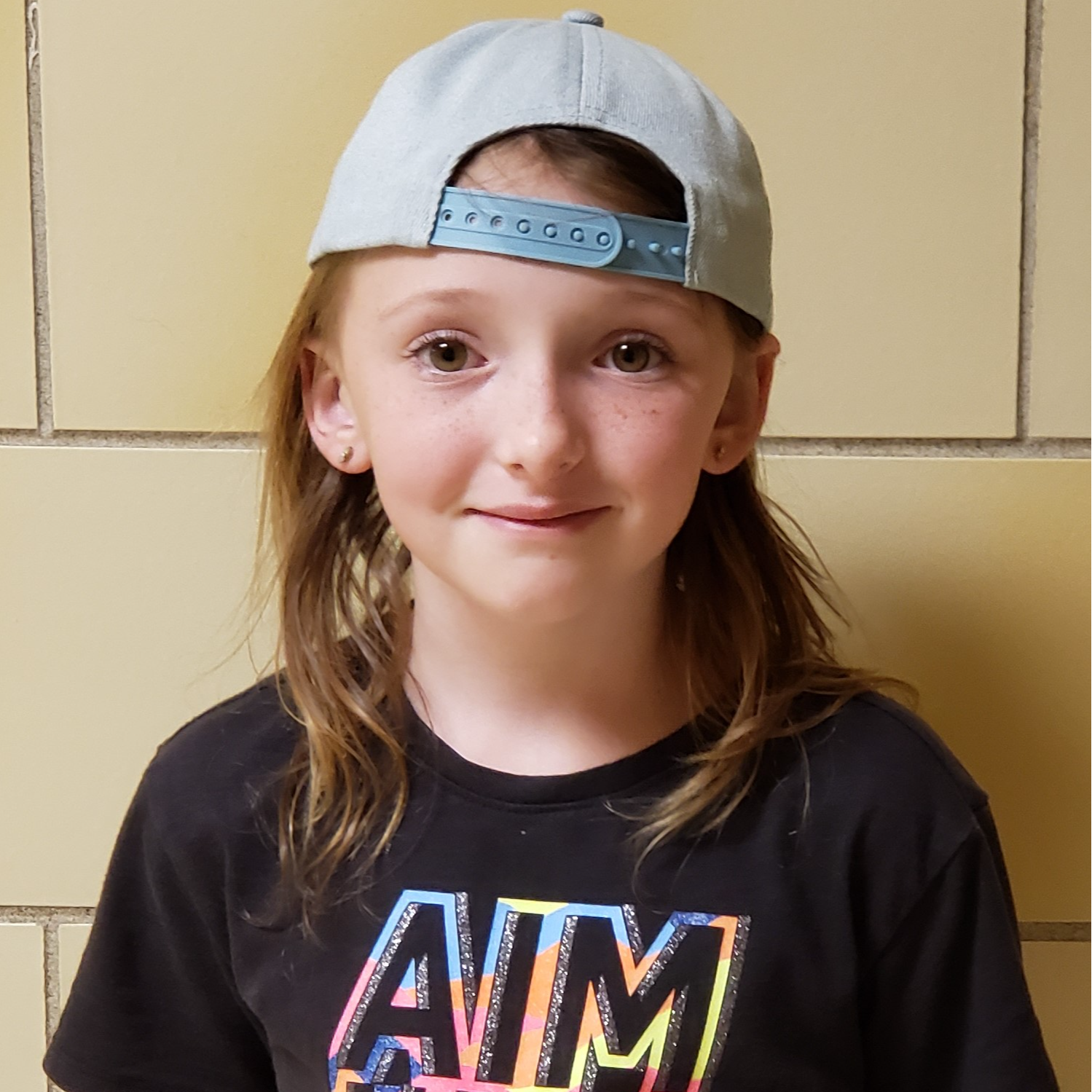 young girl with reddish hair and freckles wearing a gray cap backwards and a black t-shirt