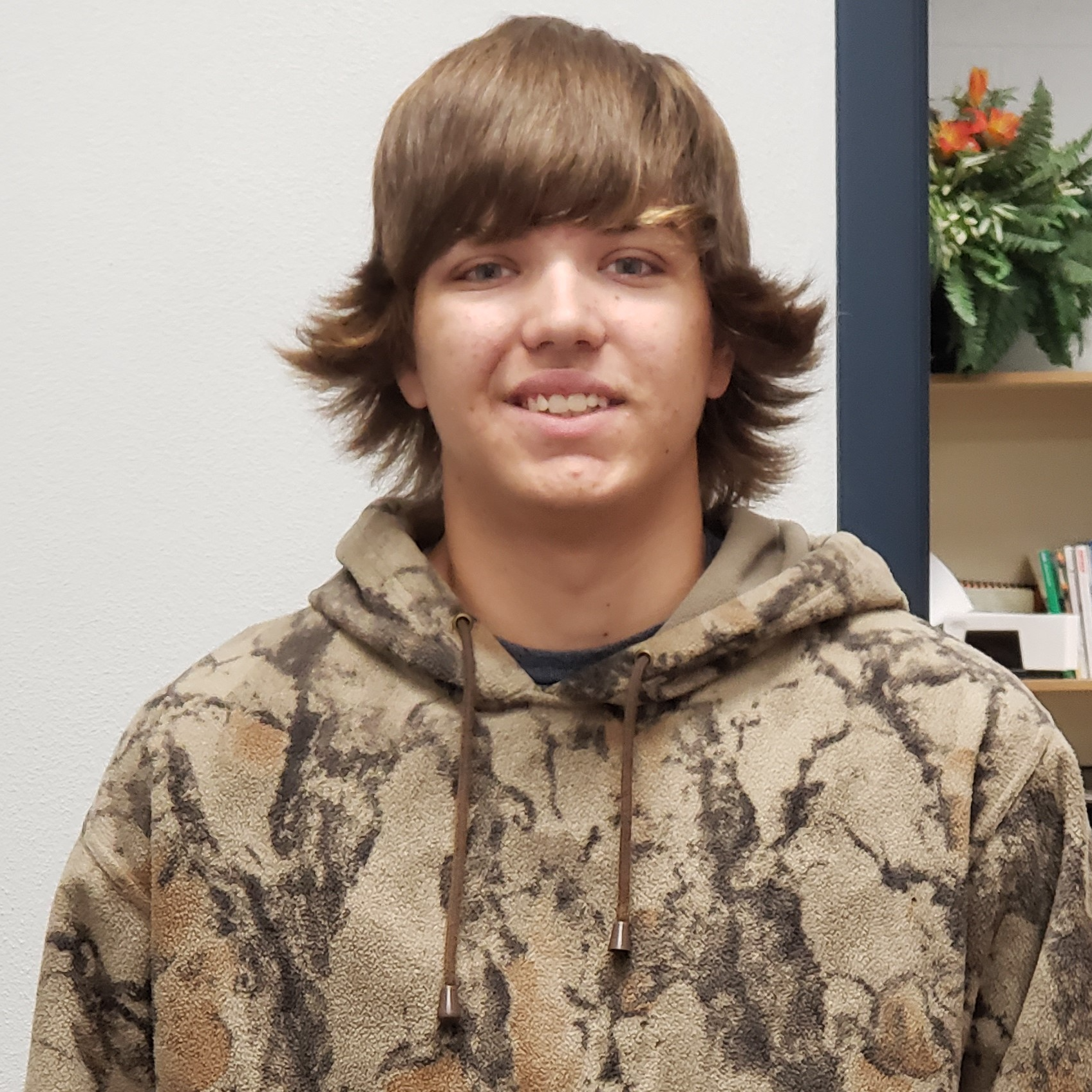 young man with light brown hair flipped up on the sides wearing a fleece camouflage hoodie