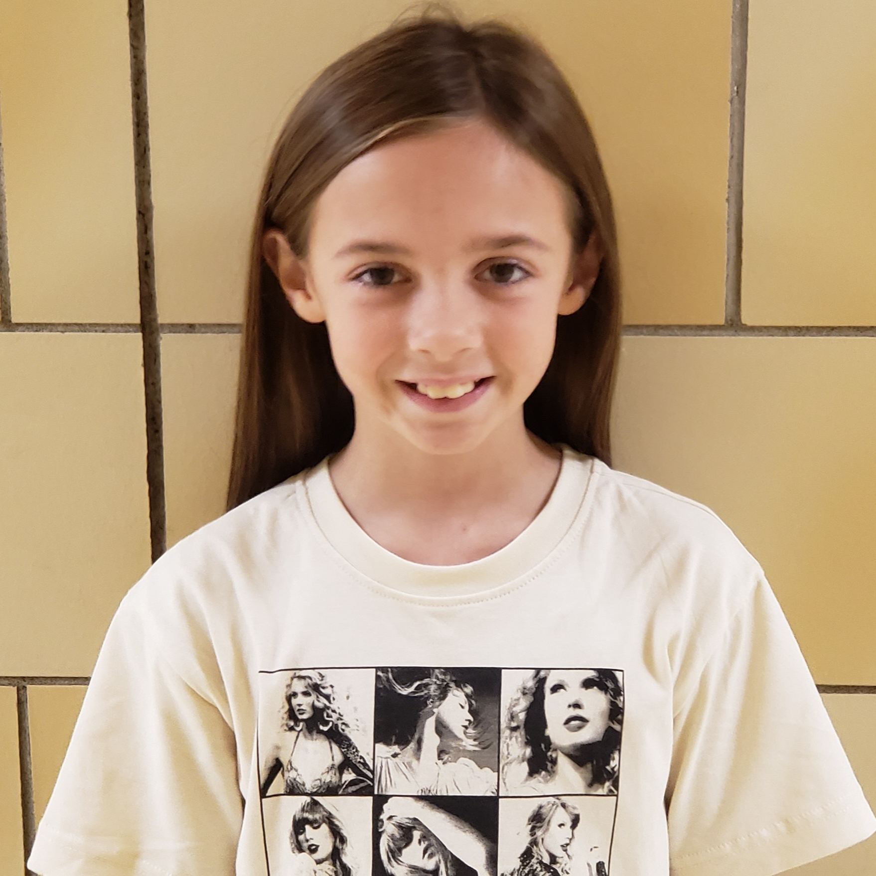 smiling girl with long brown hair wearing a cream colored Taylor Swift t-shirt