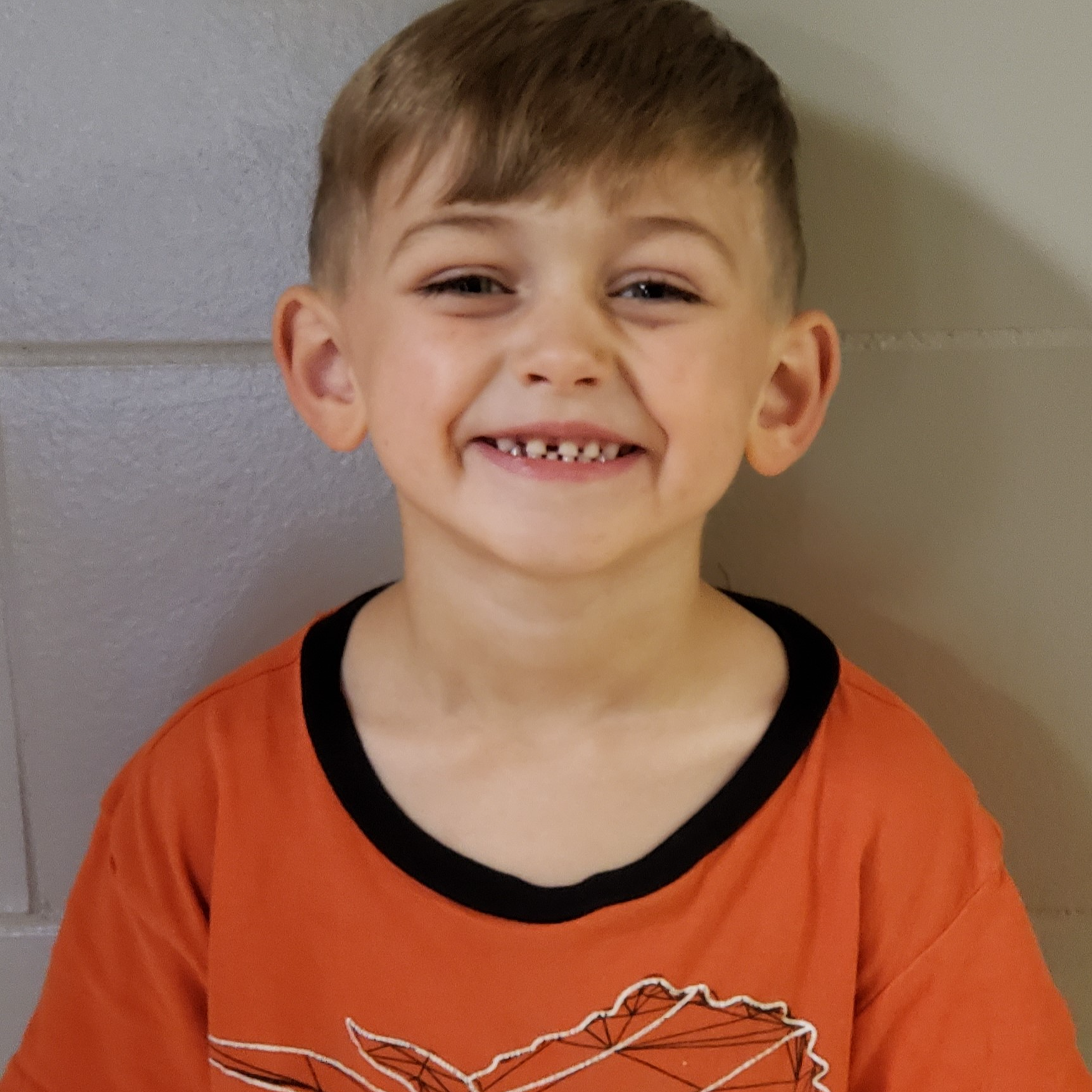 smiling young boy with light brown hair wearing a dark orange t-shirt