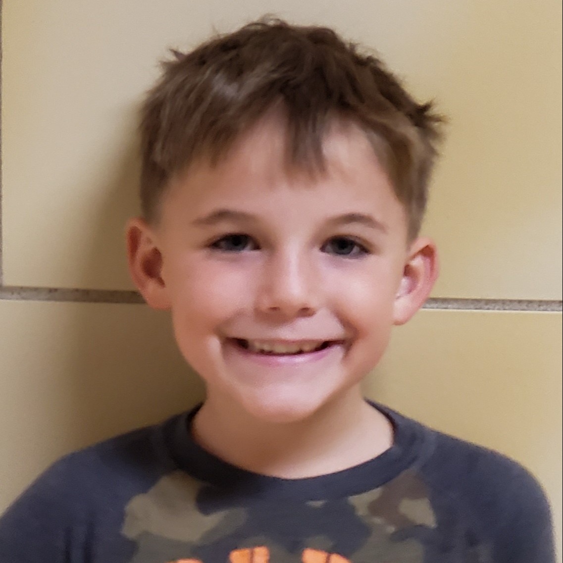 young boy with messy dark blonde hair wearing a navy and camo t-shirt