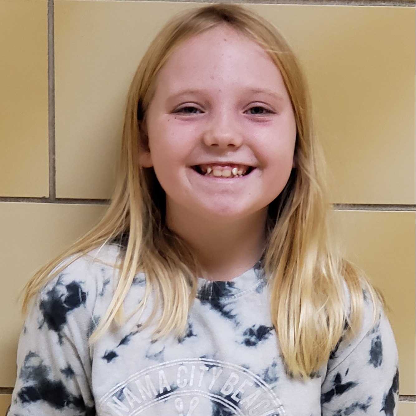 smiling girl with long blonde hair wearing a white & blue tie-dye t-shirt