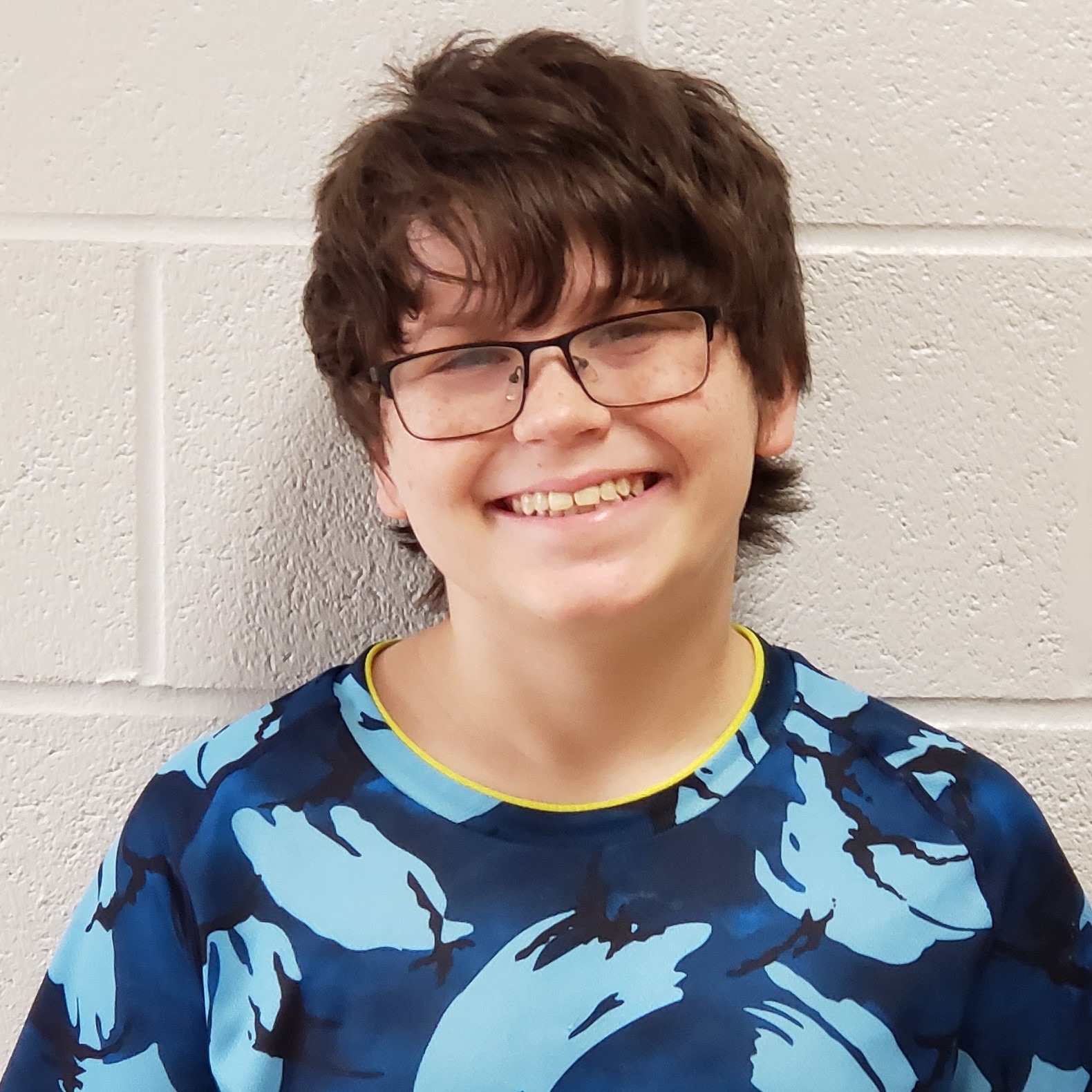 smiling boy with brown hair and glasses wearing a blue camouflage t-shirt