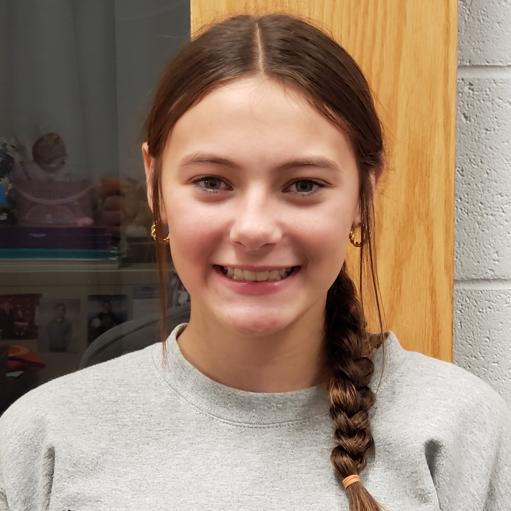 smiling young lady with brown hair in a braid wearing a gray sweatshirt  and hoop earrings