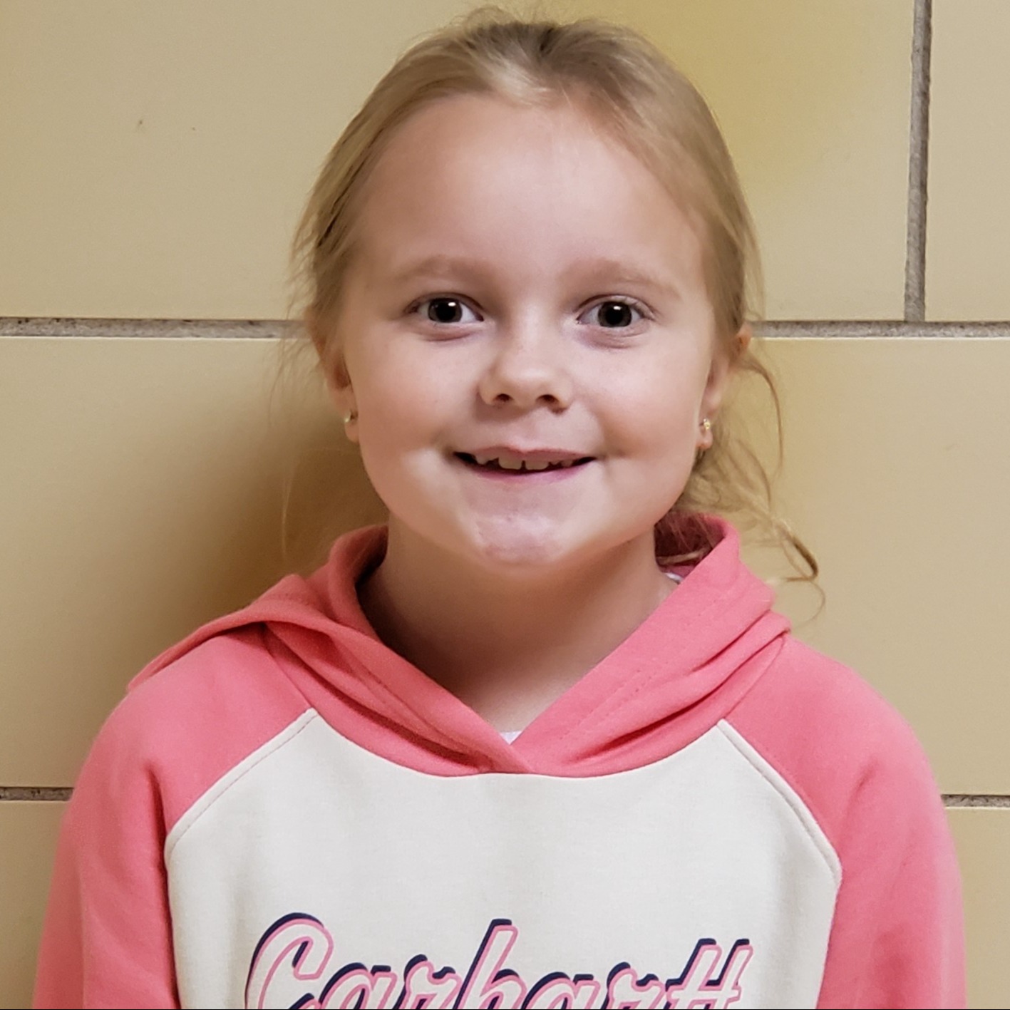 smiling girl with blonde hair pulled back wearing a pink and white hoodie