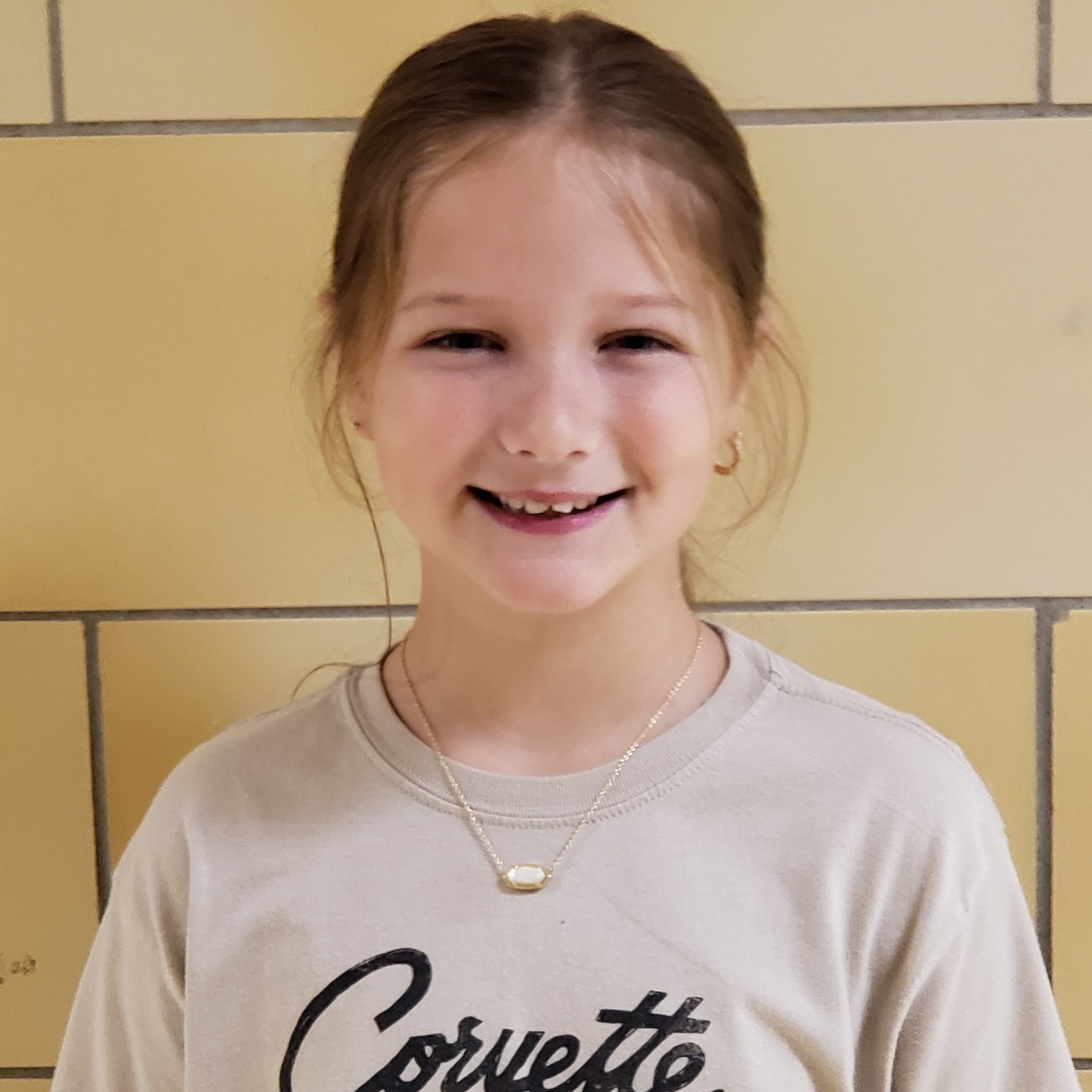 smiling girl with dark hair pulled back wearing a tan Corvette t-shirt