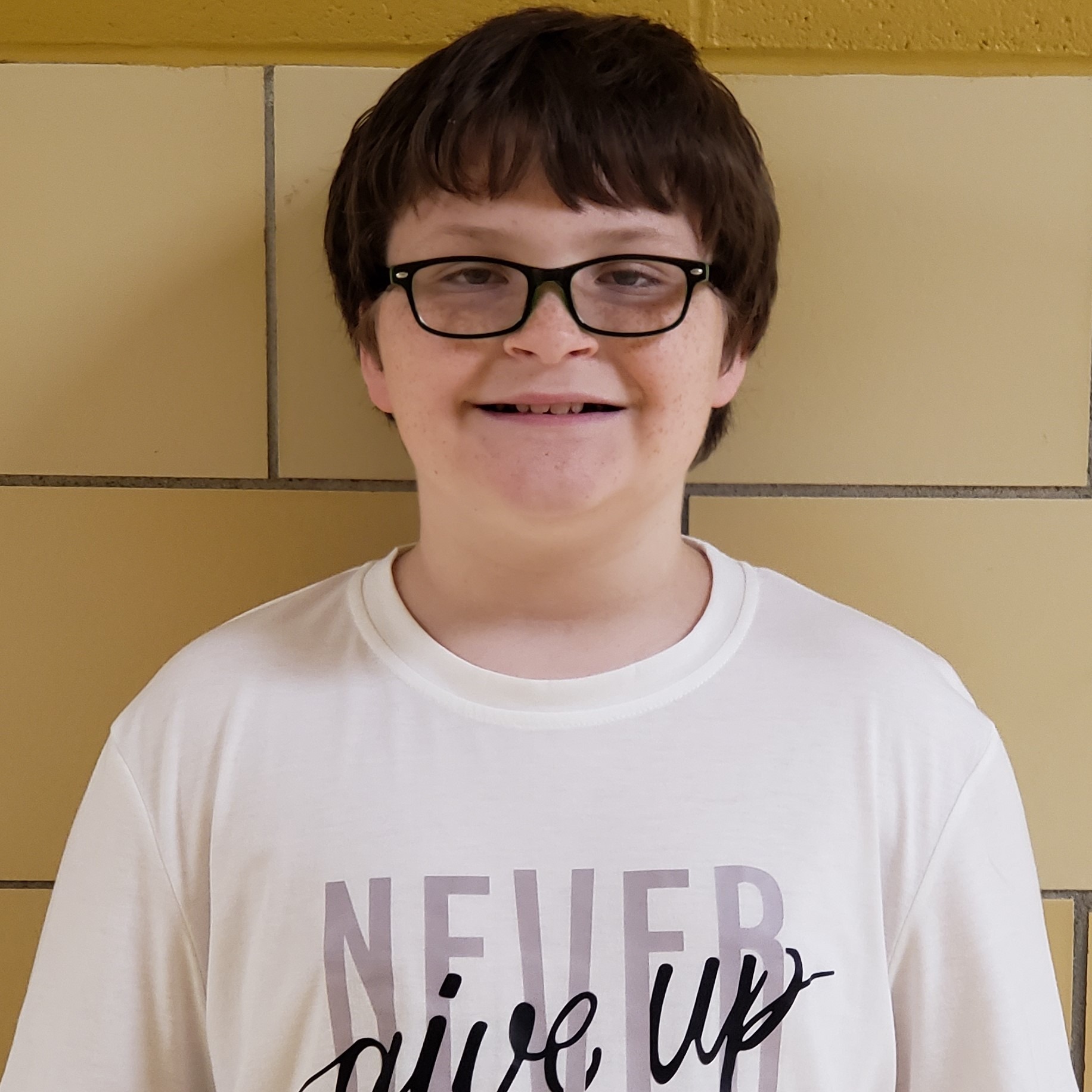 smiling boy with dark hair and freckles wearing black-rimmed glasses and a white t-shirt