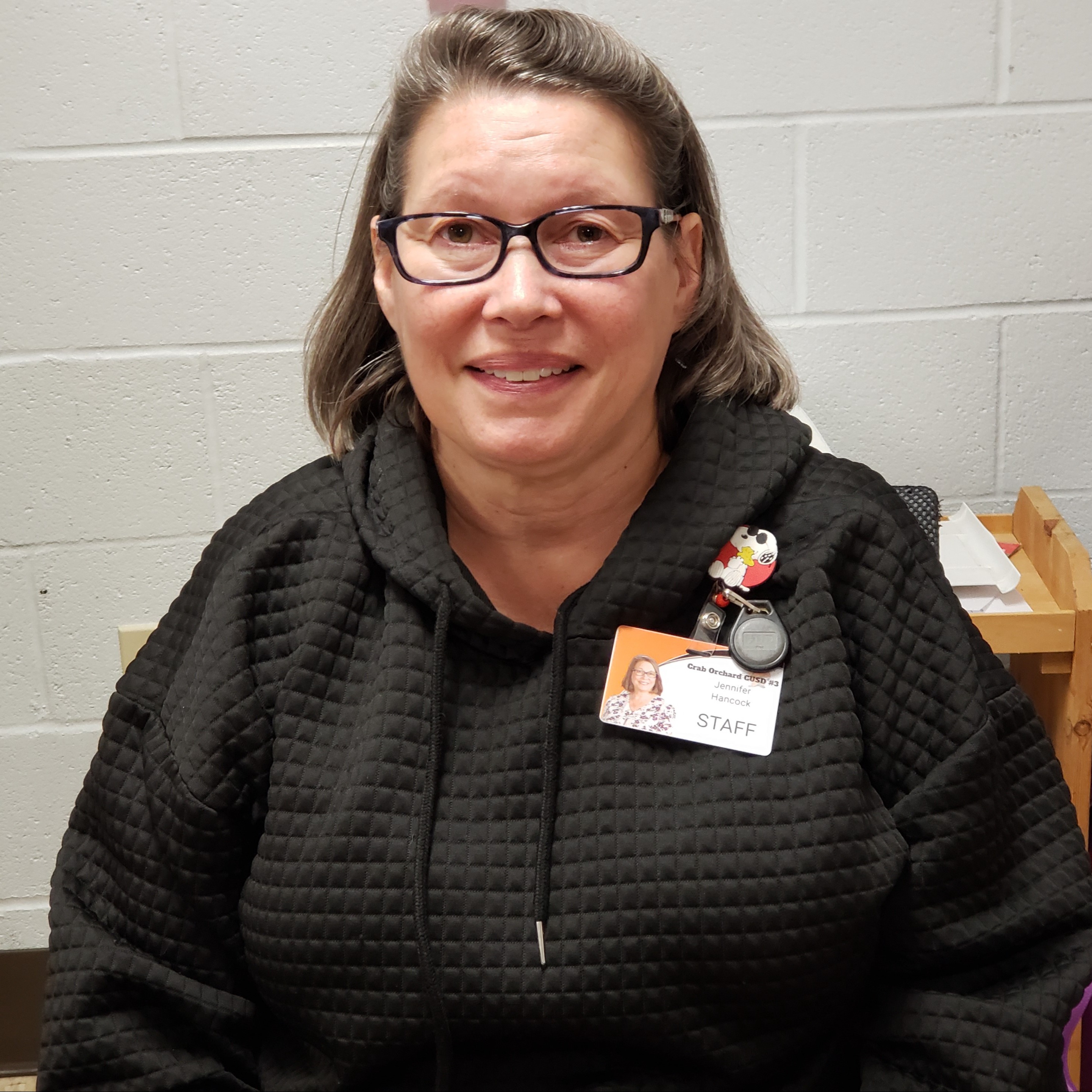 female staff member with gray hair wearing glasses, a black quilted hoodie, and a name badge