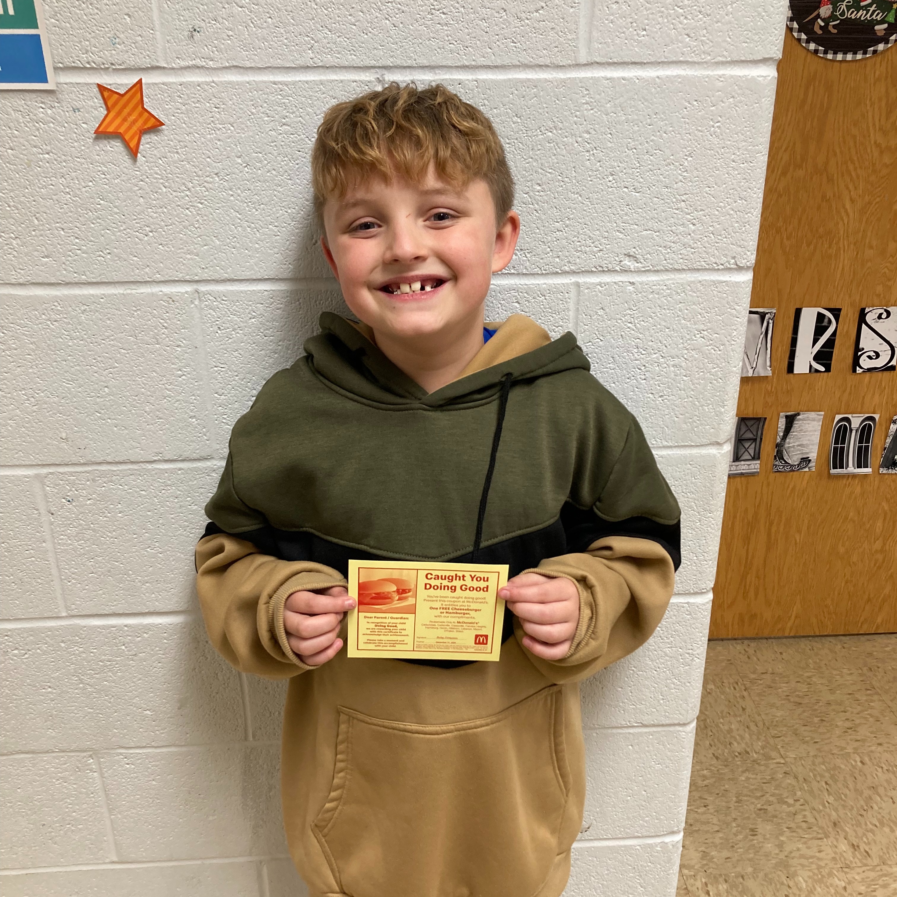 smiling boy with blonde hair wearing a green and khaki hoodie