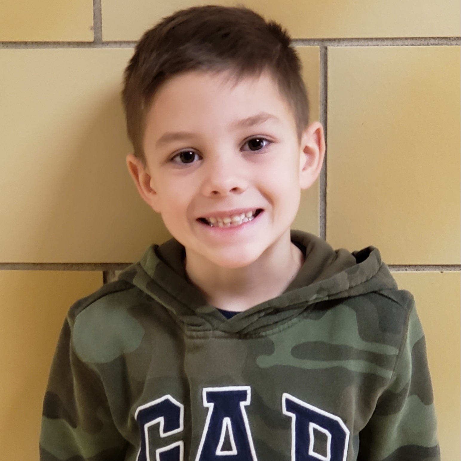 smiling young boy with dark hair wearing a camouflage hooded sweatshirt with GAP on it