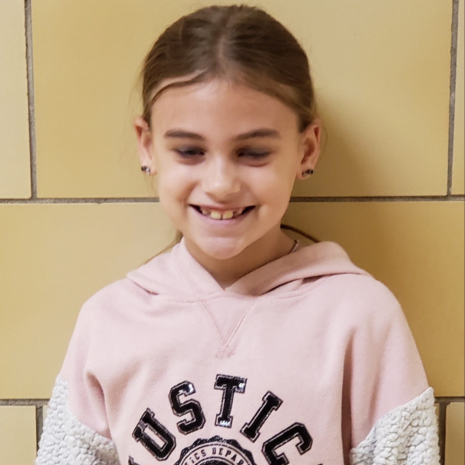 smiling girl with dark blonde hair wearing a pink hooded sweatshirt