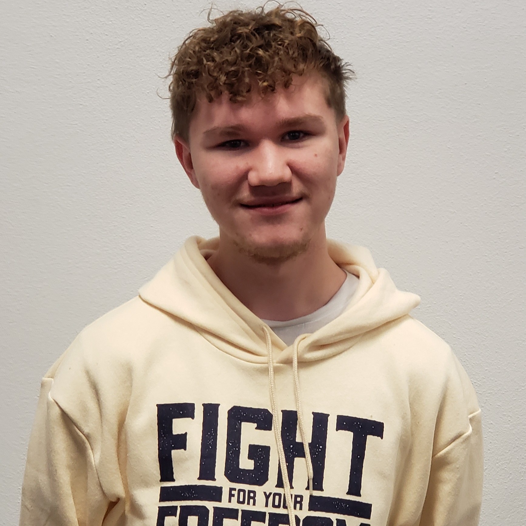 young man with dark blonde curly hair wearing a light yellow hooded sweatshirt