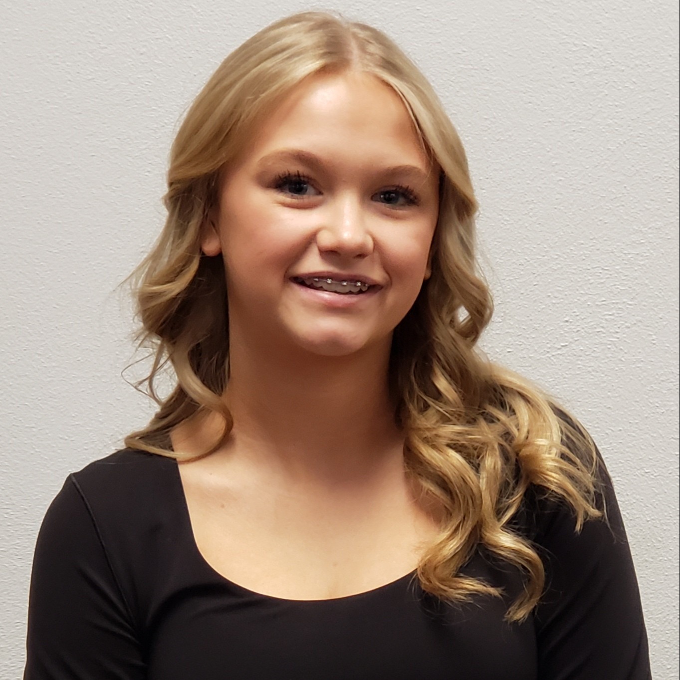 smiling young lady with braces and blonde hair in curls wearing a black t-shirt