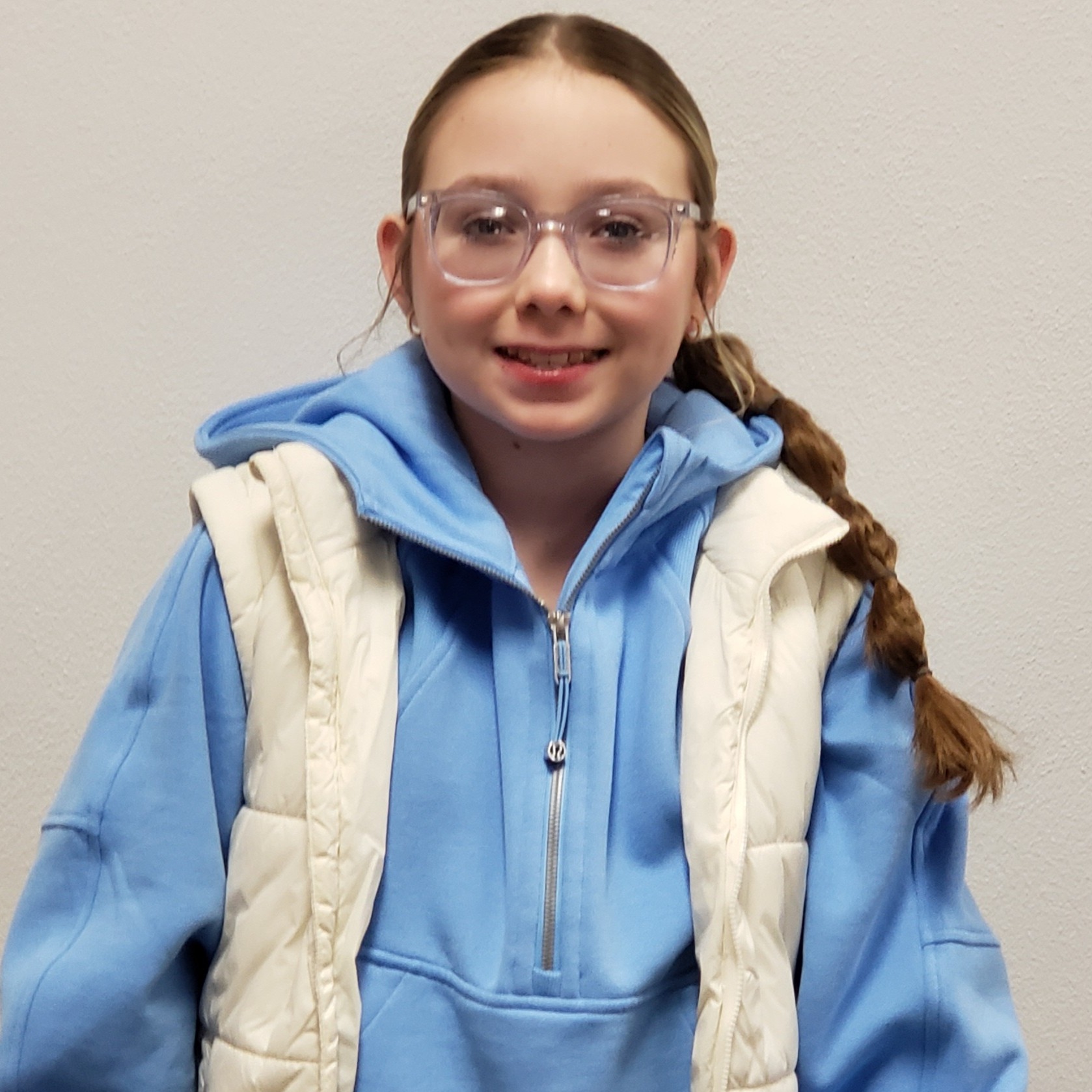 smiling young lady with glasses and brown hair pulled back wearing a light blue sweatshirt under a white vest