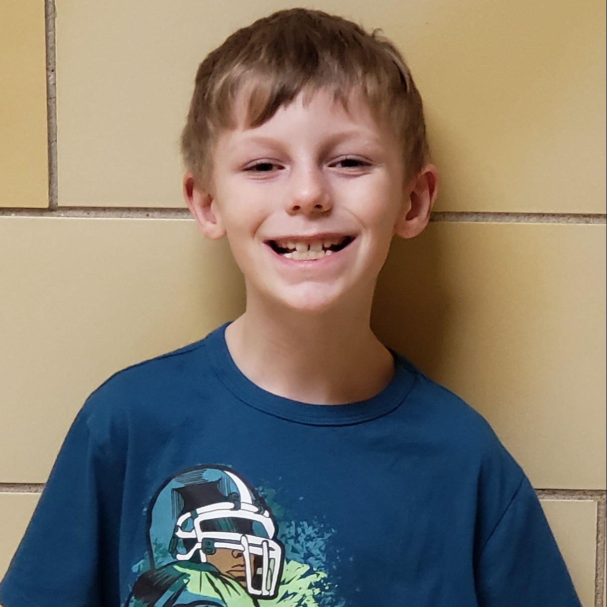 smiling boy with blonde hair wearing a blue football t-shirt