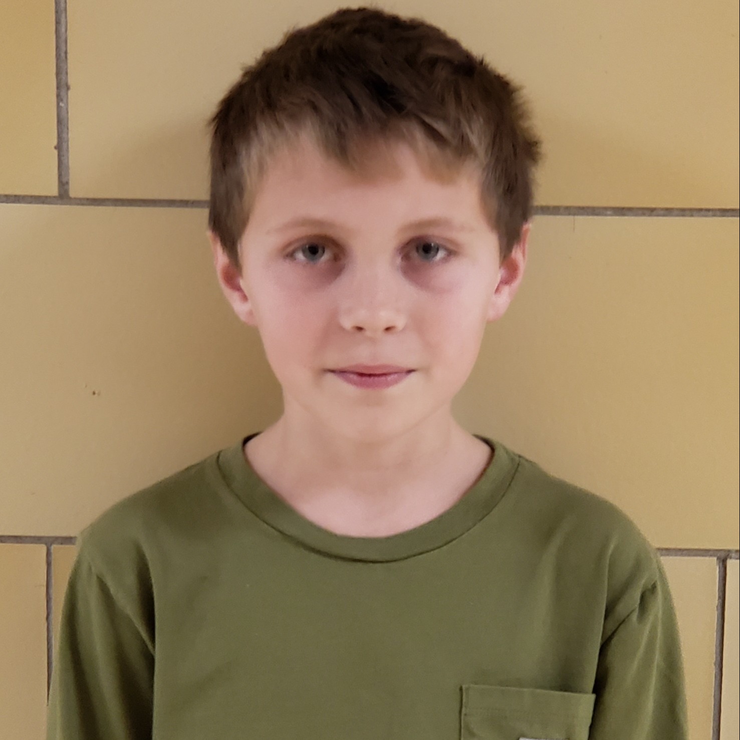 smiling young boy with dark blonde hair wearing an olive green t-shirt