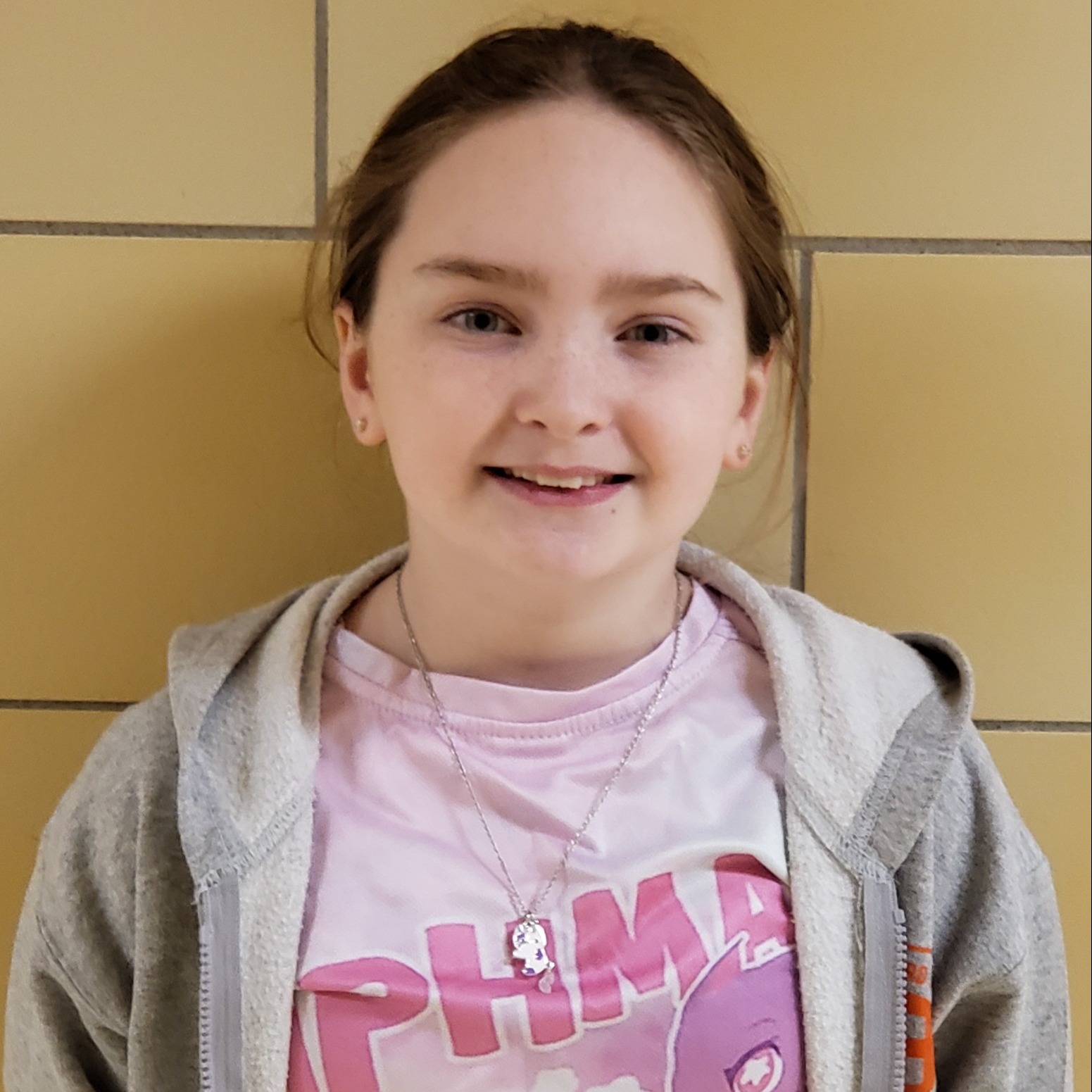 girl with reddish hair pulled back wearing a pink t-shirt under a gray jacket